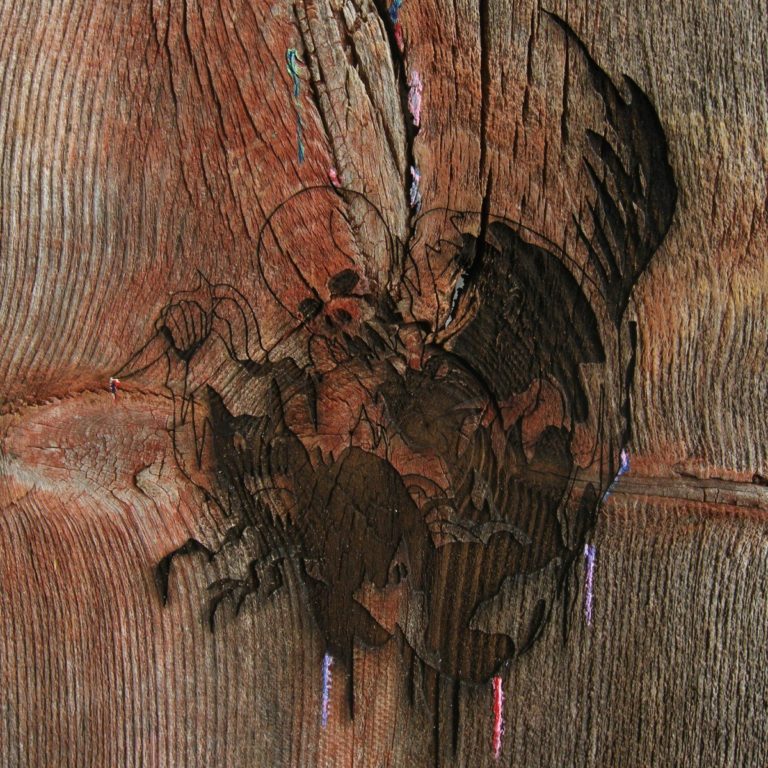 Holzstruktur mit eingravierten, abstrakten Formen und bunten Fäden.