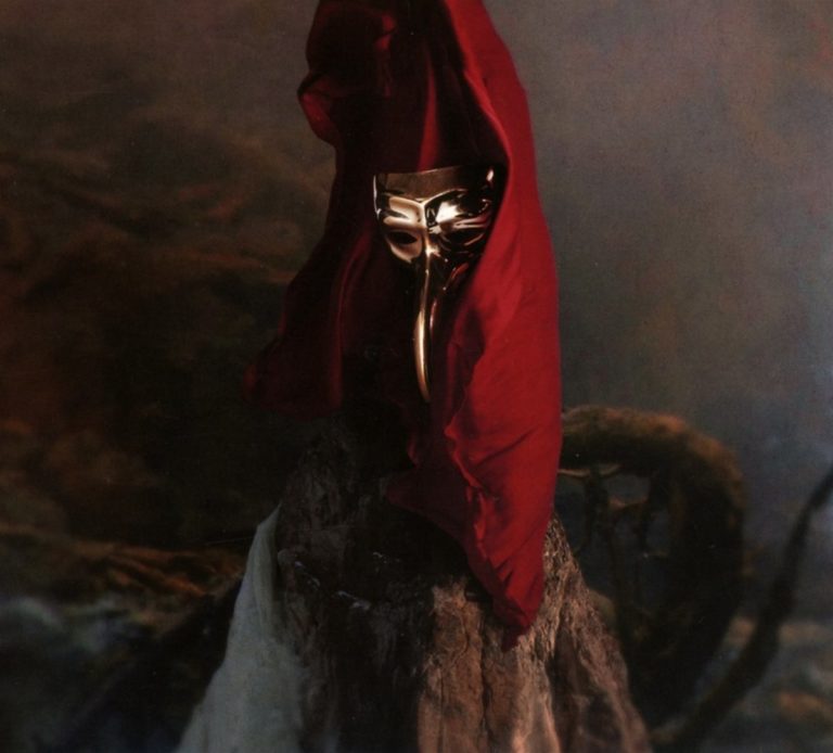 Goldene Maske unter rotem Tuch auf Felsen in mystischer Umgebung.