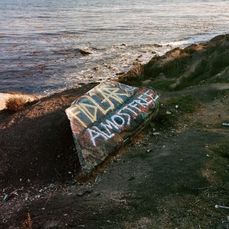 Felsen am Meer mit Graffiti-Schriftzug FIDLAR ALMOST FREE.