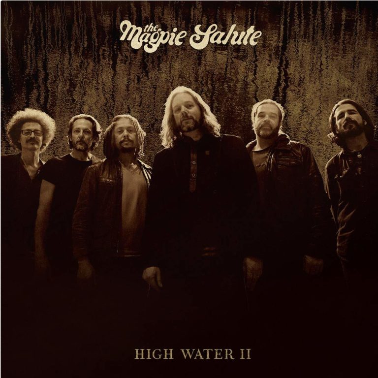 Sechs Bandmitglieder von The Magpie Salute stehen vor einem dunklen Hintergrund.