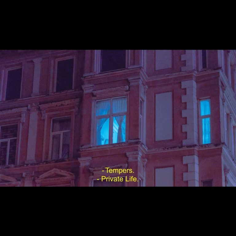 Fassade eines Gebäudes bei Nacht mit blau beleuchtetem Fenster.