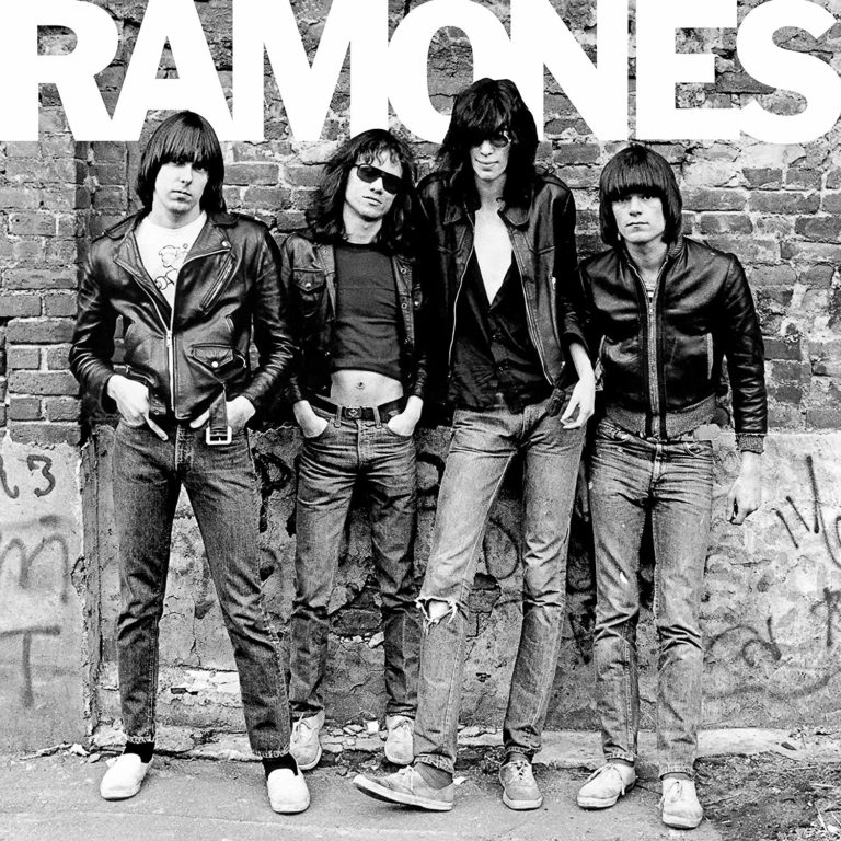 Die Ramones posieren in Lederjacken vor einer Backsteinmauer.