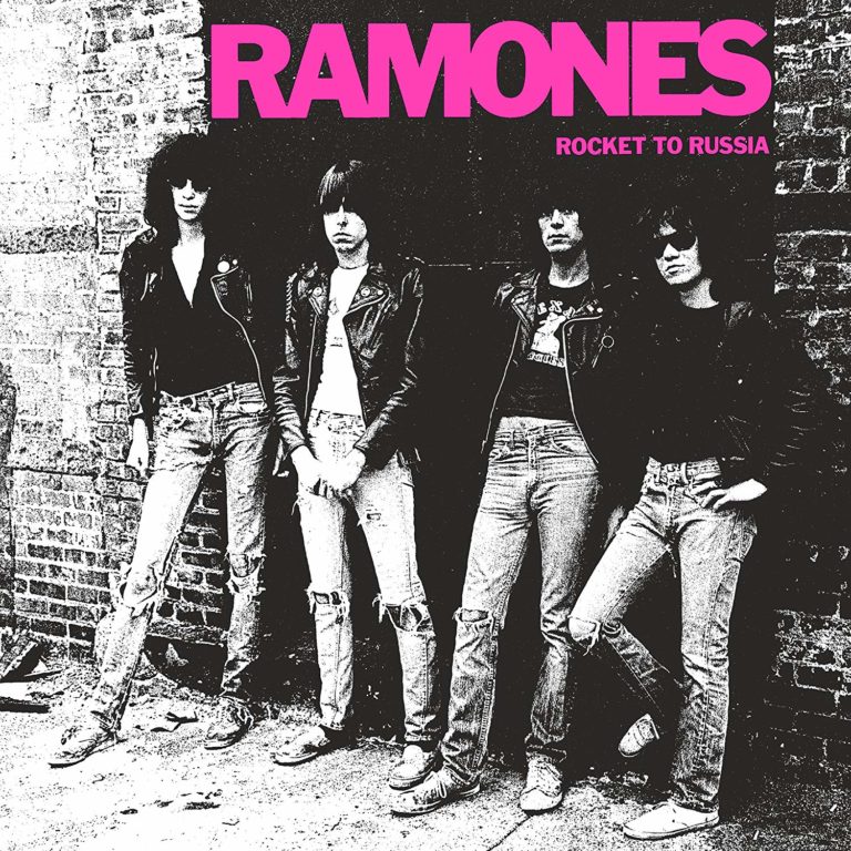 Die Ramones posieren vor einer Backsteinmauer in Lederjacken und zerrissenen Jeans.