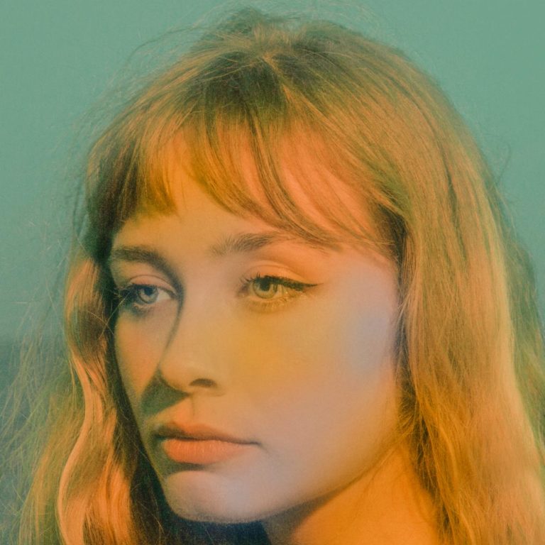 Porträt einer Frau mit langen Haaren und melancholischem Blick vor unscharfem Hintergrund.
