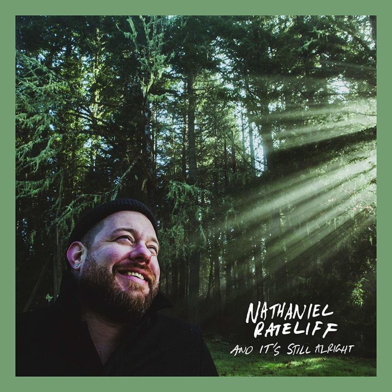 Mann mit Bart lächelt im Wald, Sonnenstrahlen durchbrechen die Bäume.