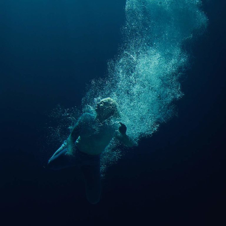 Person unter Wasser mit aufsteigenden Luftblasen in dunkler Umgebung.