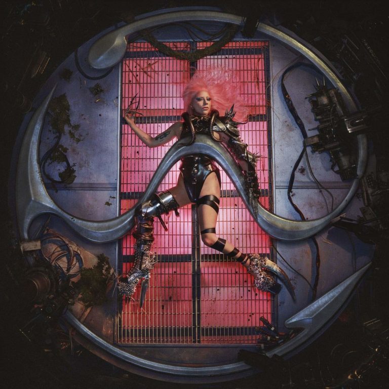 Lady Gaga mit pinkem Haar in futuristischer Rüstung, liegend in einem kreisrunden metallischen Rahmen auf dem Albumcover zu Chromatica.