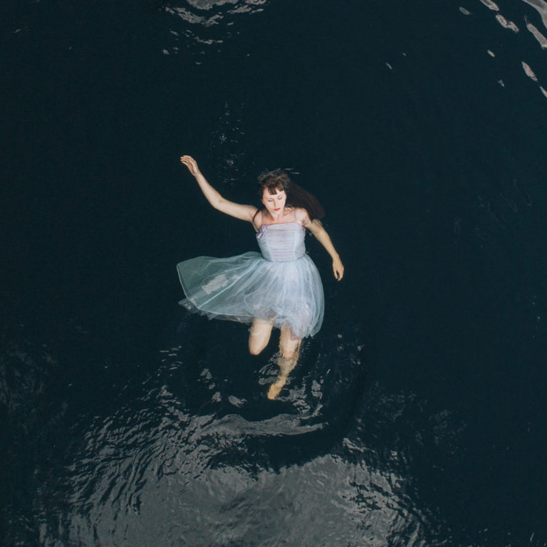 Frau in blauem Kleid schwebt auf dunklem Wasser.