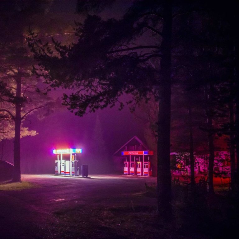 Nachtaufnahme einer beleuchteten Tankstelle im Wald mit Neonlichtern