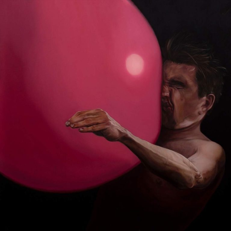 Mann drückt Gesicht gegen großen rosa Ballon in dunkler Umgebung.