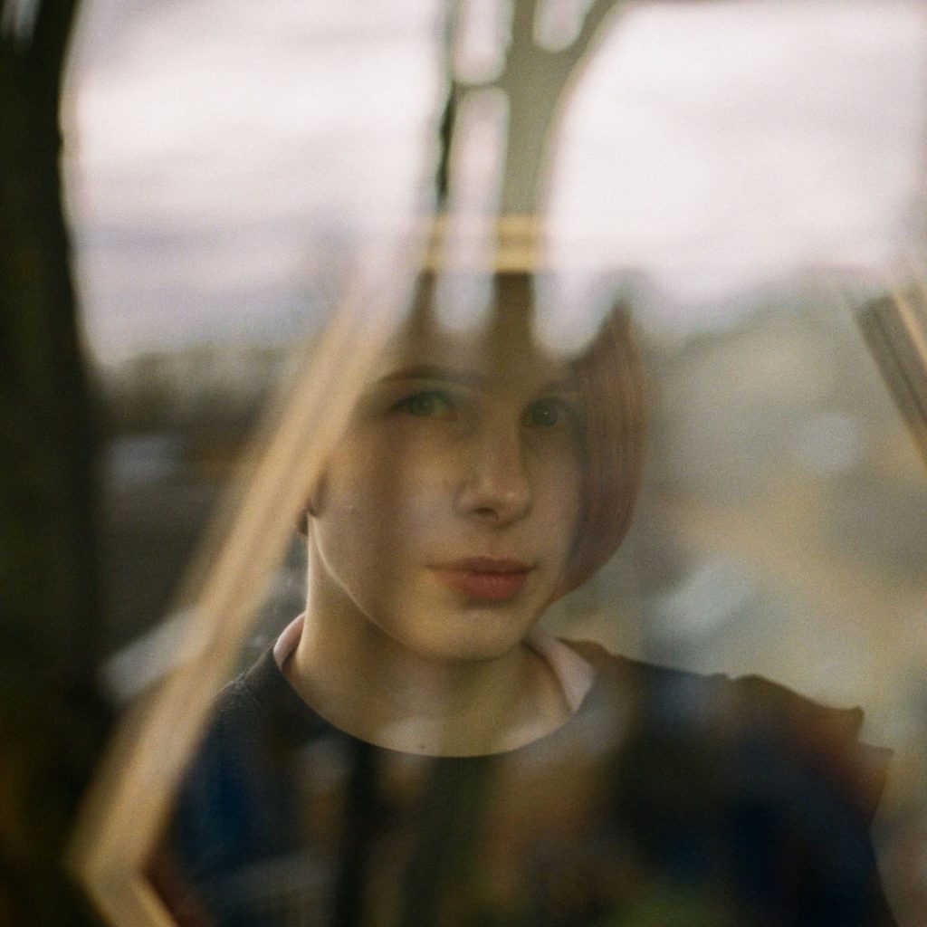 Porträt einer Person hinter einem Fenster mit verschwommenem Hintergrund.