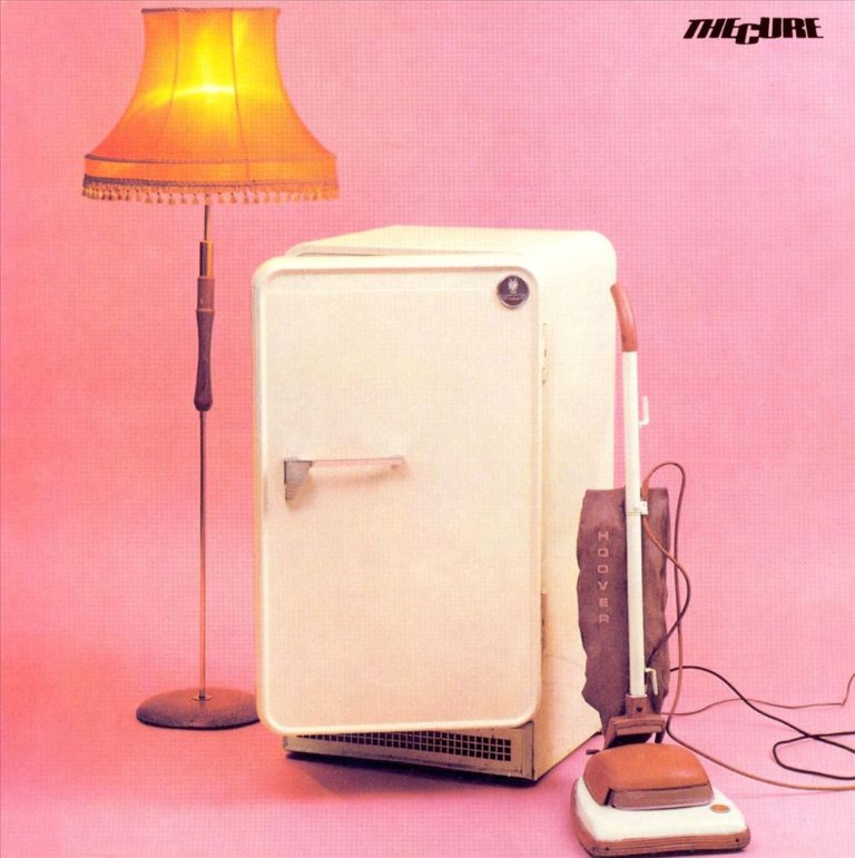 Ein Kühlschrank und ein Staubsauger stehen neben einer Lampe vor einem pinken Hintergrund.
