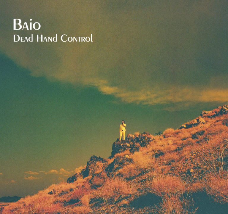 Albumcover von Baio – Dead Hand Control: Eine einzelne Person in heller Kleidung steht auf einem felsigen, ockerfarbenen Hügel unter einem dramatisch grün-goldenen Himmel.