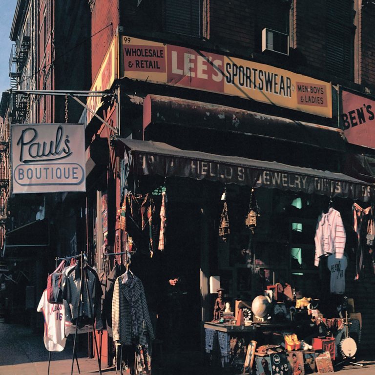 Ladenfront mit dem Schild Pauls Boutique und verschiedenen Kleidungsstücken auf der Straße.