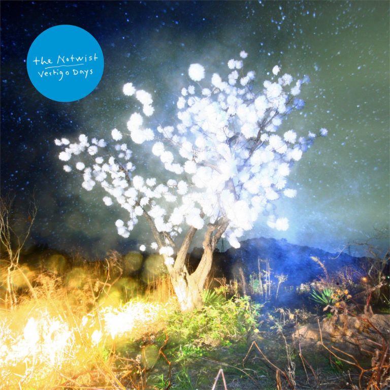 Albumcover von The Notwist „Vertigo Days“ mit einem leuchtenden weißen Baum in nächtlicher Landschaft, umgeben von Lichtreflexen und Sternenhimmel.