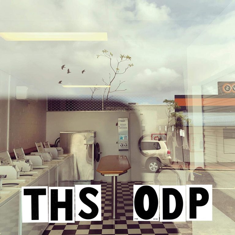 Blick durch eine Glasfront in einen Waschsalon mit kariertem Boden. Spiegelung von Himmel und Vögeln, große Lettern „THS ODP“ im Vordergrund – urban und melancholisch.