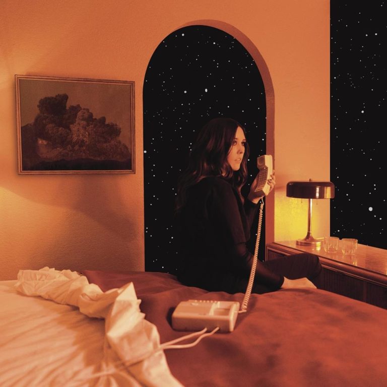 Eine Frau sitzt nachts in einem orange beleuchteten Schlafzimmer am Fenster, telefoniert und blickt hinaus in den Sternenhimmel – melancholische Retro-Stimmung mit Blick ins All.