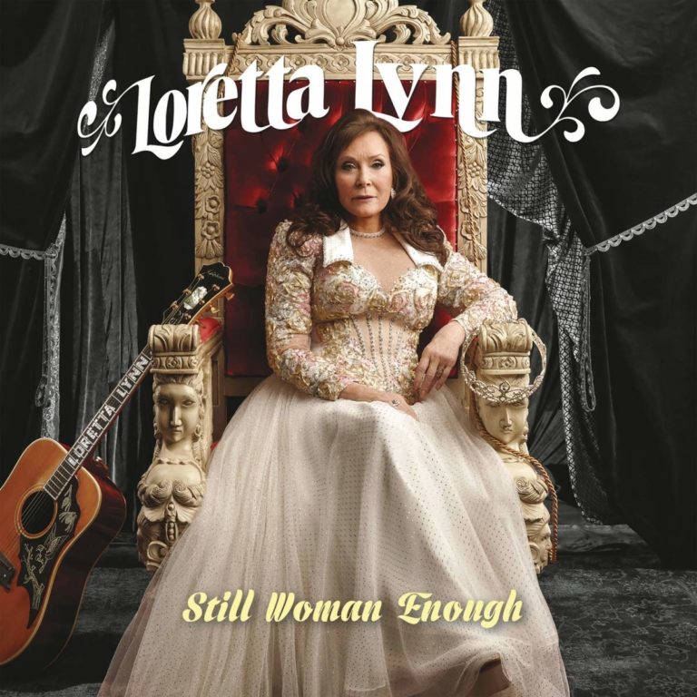 Loretta Lynn sitzt in einem prunkvollen Thronsessel mit rotem Samtbezug, umgeben von dunklen Vorhängen und einer Gitarre mit ihrem Namen, gekleidet in ein opulentes Kleid mit floralen Verzierungen – eine majestätische Pose zwischen Country-Ikone und Königin.