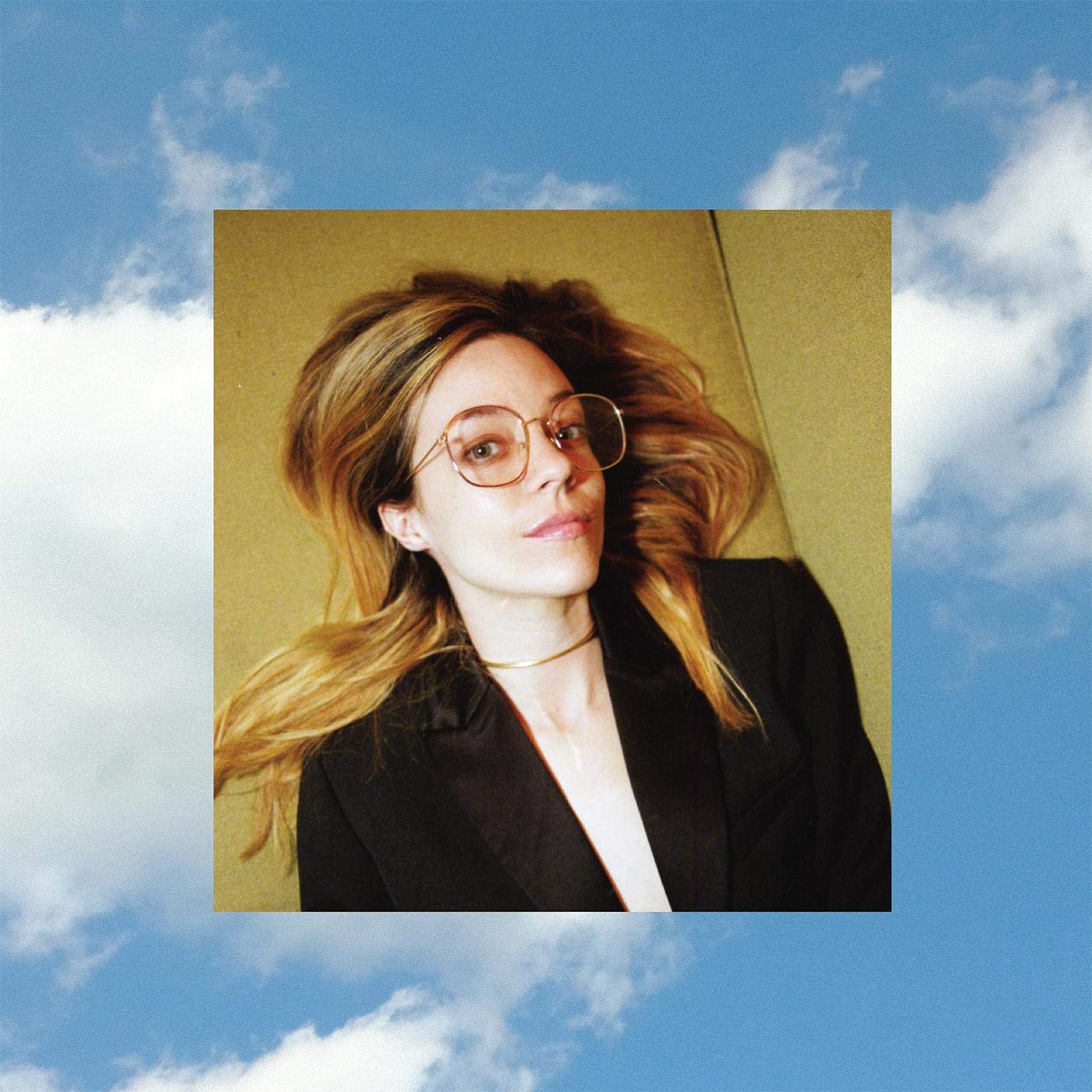 Cover von Anna Fox Rochinskis Album Cherry: Die Künstlerin liegt in Blazer und Brille auf hellem Untergrund, das Bild schwebt vor blauem Himmel mit Wolken.