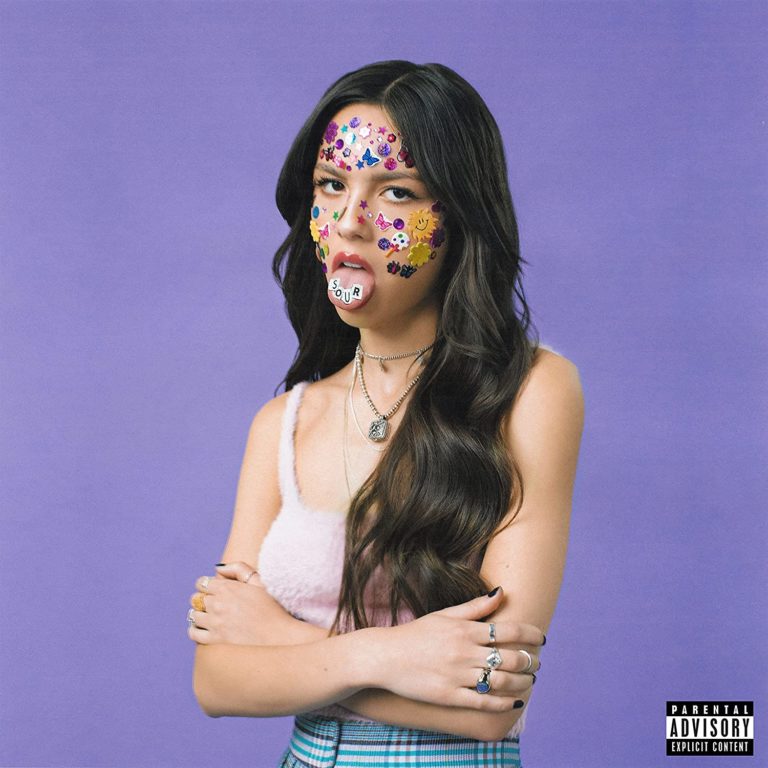 Albumcover von Olivia Rodrigos „SOUR“: Die Künstlerin steht vor lila Hintergrund, mit bunten Stickern im Gesicht und einer Zunge, auf der Buchstabenwürfel das Wort „SOUR“ zeigen. Sie schaut trotzig in die Kamera, die Arme verschränkt.