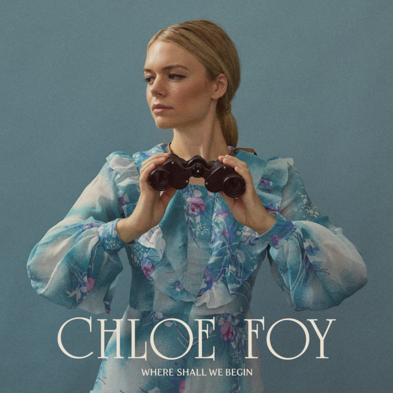Chloe Foy auf dem Cover von „Where Shall We Begin“, in floralem Kleid mit Fernglas vor blauem Hintergrund, verträumt zur Seite blickend.