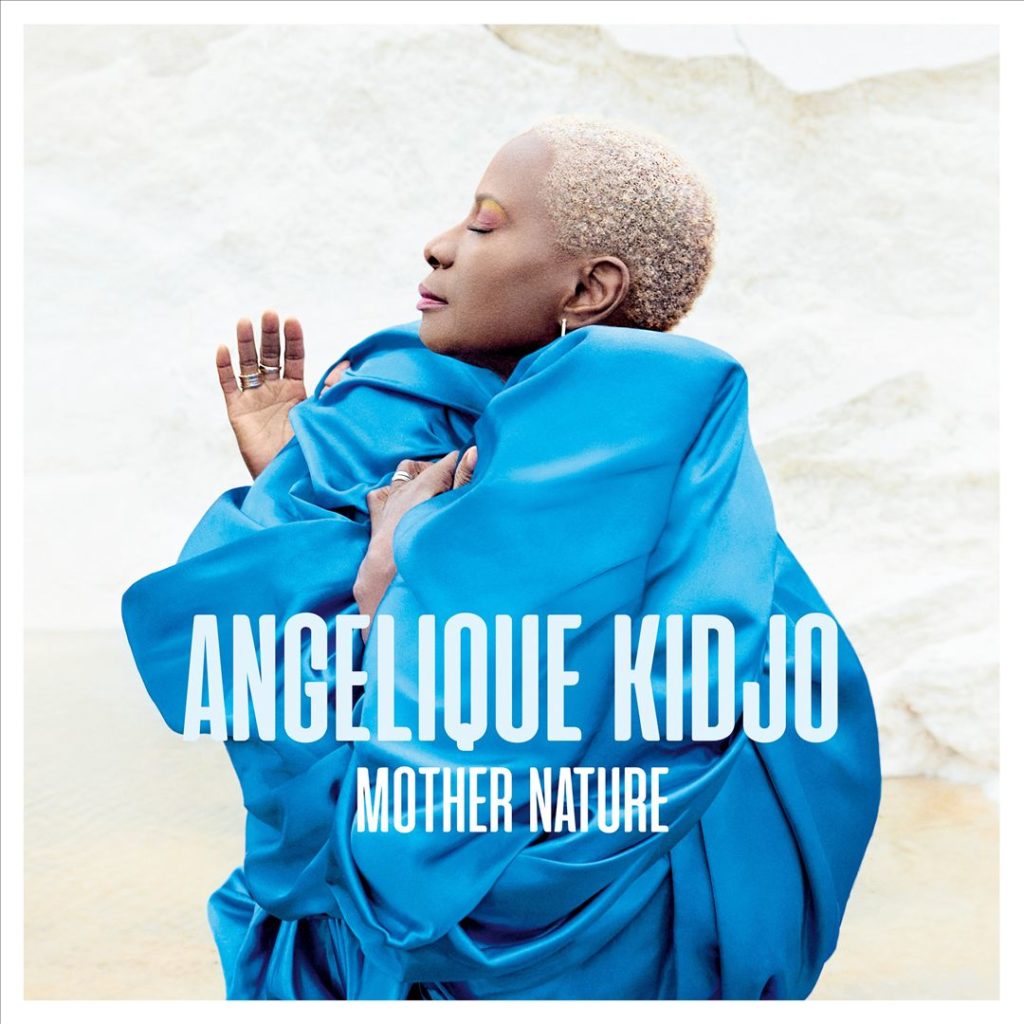 Angélique Kidjo in leuchtend blauem Gewand vor heller Naturkulisse – Albumcover zu „Mother Nature“ mit stolzer Pose und geschlossenen Augen.