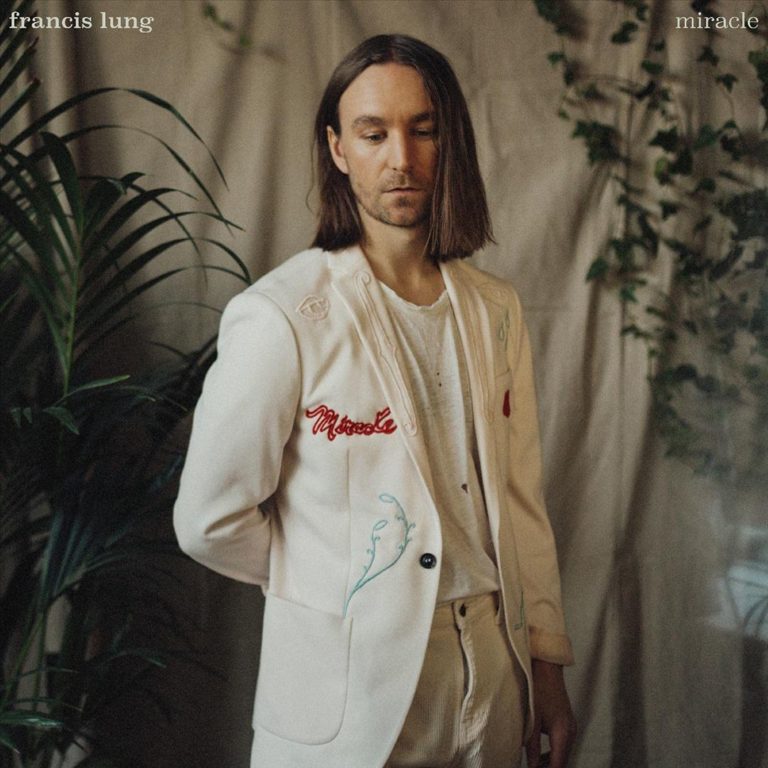 Francis Lung im cremefarbenen Anzug vor Pflanzen und Stoffkulisse – verträumtes Porträt zum introspektiven Pop-Album „Miracle“.