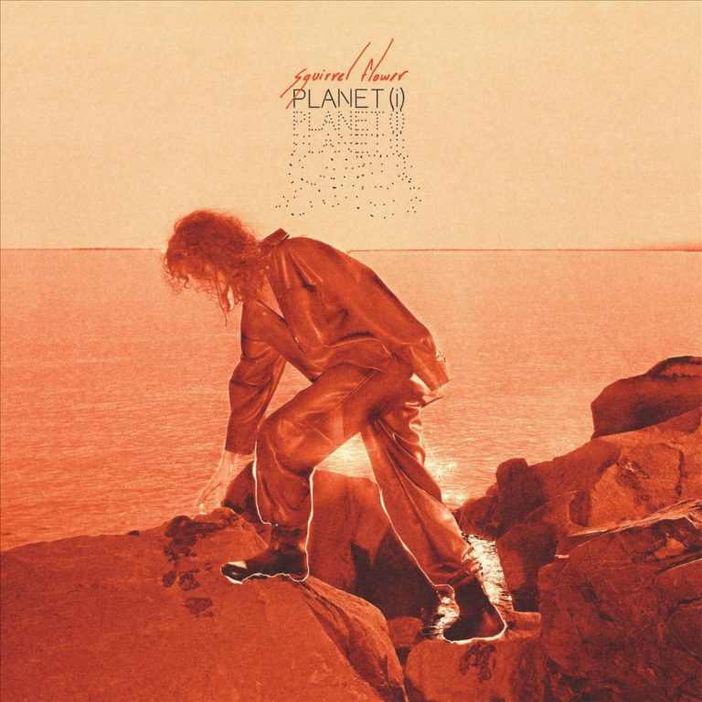 Das Albumcover von „Planet (i)“ von Squirrel Flower zeigt die Künstlerin in rostfarbenem Licht auf Felsen am Meer – eine surreale, apokalyptisch wirkende Szene.
