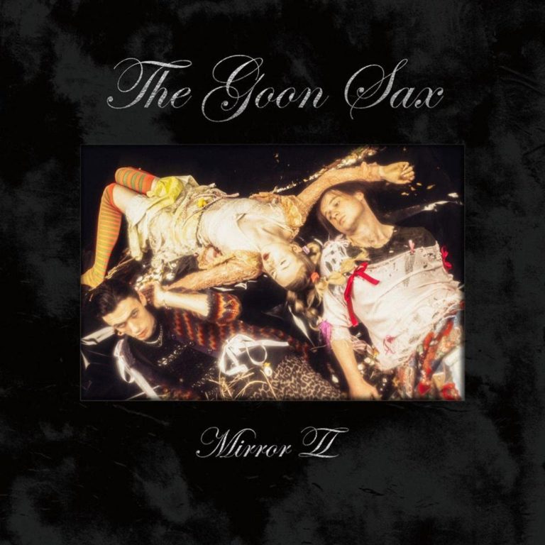 Albumcover von The Goon Sax – Mirror II: Drei Personen in extravagantem Outfit liegen wie entrückt auf dunklem Untergrund, umgeben von Glitzer, Konfetti und Unschärfe.