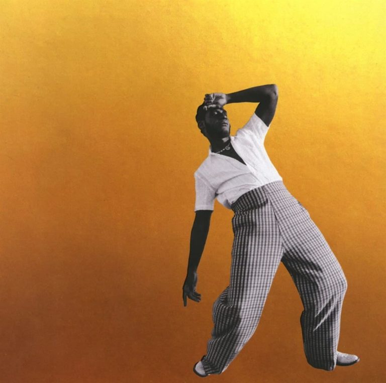 Leon Bridges posiert in einer dramatisch geschwungenen Haltung vor einem goldgelben Hintergrund. Sein Outfit kombiniert eine weite, karierte Hose mit offenem weißen Hemd – retro und stilvoll zugleich. Die Pose erinnert an einen eingefrorenen Tanzmoment, mitten in der Bewegung.