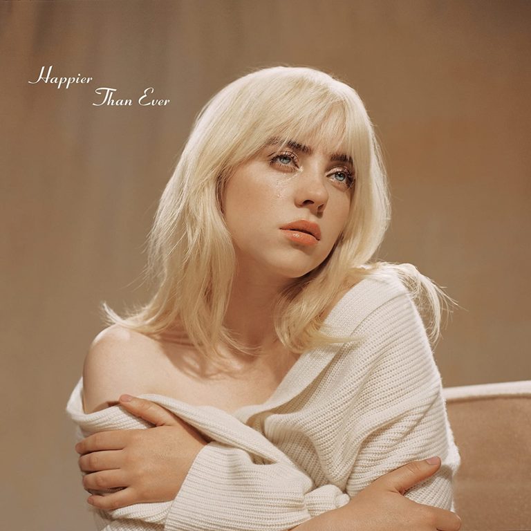 Billie Eilish mit blondem Haar, in einem cremefarbenen Strickpullover, sitzt nachdenklich mit verschränkten Armen und Tränen im Gesicht vor weichem, beigefarbenem Hintergrund. Schriftzug: „Happier Than Ever“.