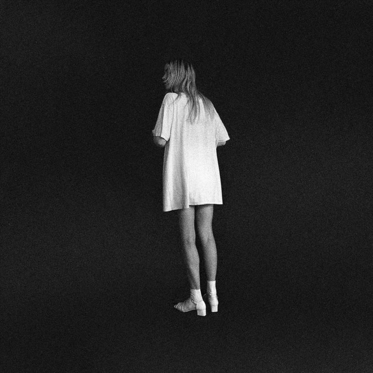 Schwarz-weißes Coverbild von Bnny – eine Frau mit langen Haaren steht rückwärtsgewandt und verloren in einem leeren, dunklen Raum. Sie trägt ein übergroßes T-Shirt und helle Socken mit Absatzschuhen. Eine stille, fragile Szene.