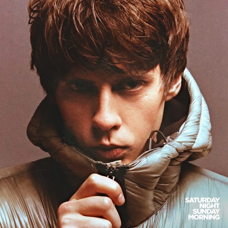 Albumcover von Jake Bugg „Saturday Night, Sunday Morning“: Nahaufnahme des Künstlers im Daunenjackenkragen, ernster Blick, gedeckte Farben.