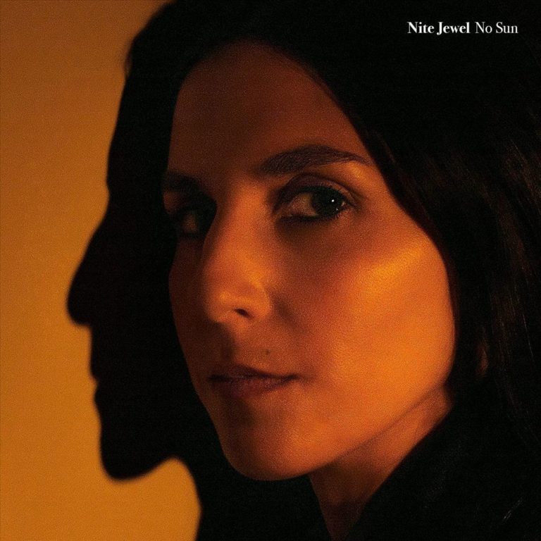 Close-up von Nite Jewel im warmen Licht, das ihr Gesicht zur Hälfte beleuchtet. Ihr Schatten fällt prägnant auf die Wand – ein minimalistisches, stimmungsvolles Porträt.