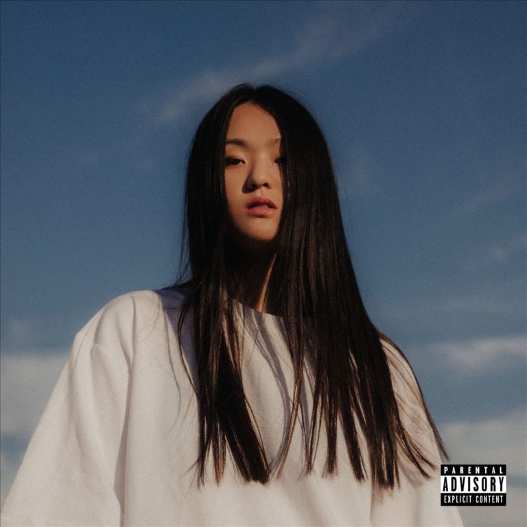 Porträt von Park Hye Jin vor einem blauen Himmel, mit ernstem Blick, glattem schwarzen Haar und weißem oversized Shirt.