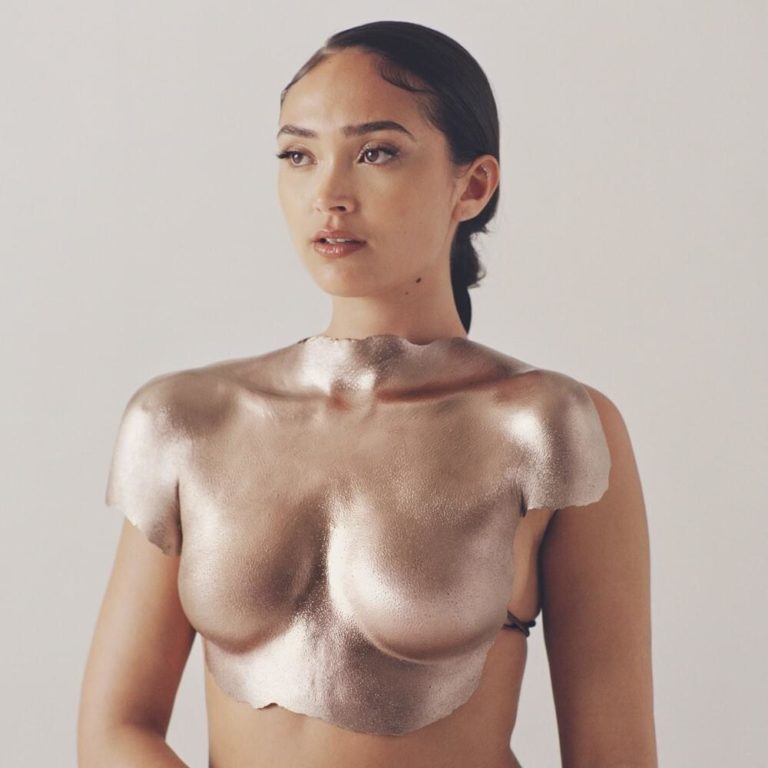 Albumcover von Joy Crookes – „Skin“: Die Künstlerin blickt ruhig nach vorn, ihr Oberkörper ist mit einer glänzenden, bronzefarbenen Rüstungsskulptur überzogen.