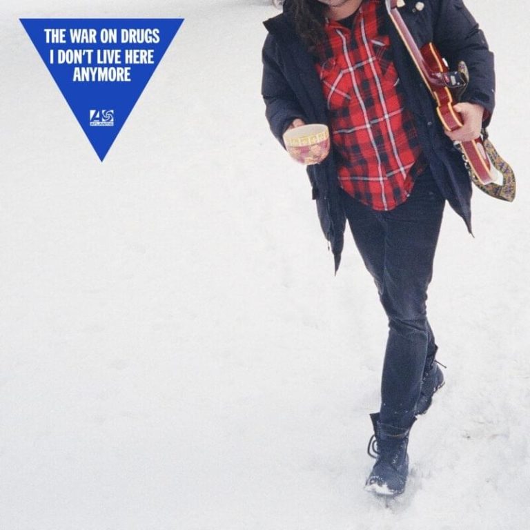 Ein Mann in dunkler Kleidung mit Gitarre und Kaffeebecher geht durch weißen Schnee – Albumcover von I Don’t Live Here Anymore von The War on Drugs.