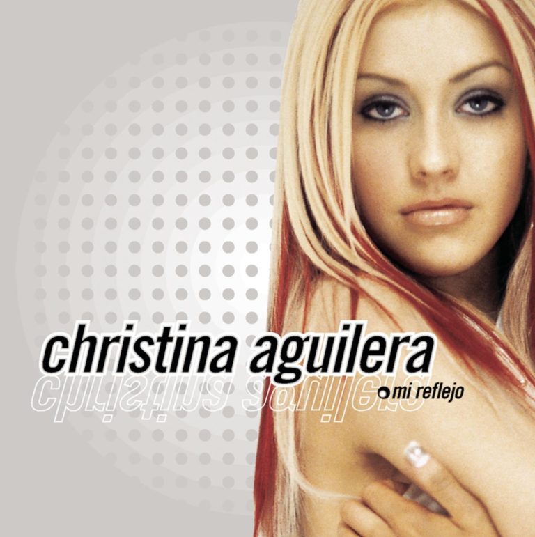 Christina Aguilera mit langen Haaren und neutralem Gesichtsausdruck vor grauem Hintergrund.