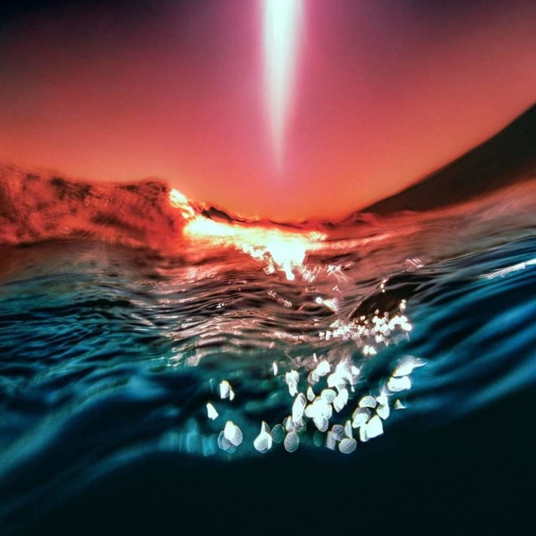 Surreale Nahaufnahme von Wasseroberfläche bei Sonnenuntergang in lebendigen Blau- und Orangetönen, reflektierende Lichtpunkte erzeugen traumhafte Atmosphäre.