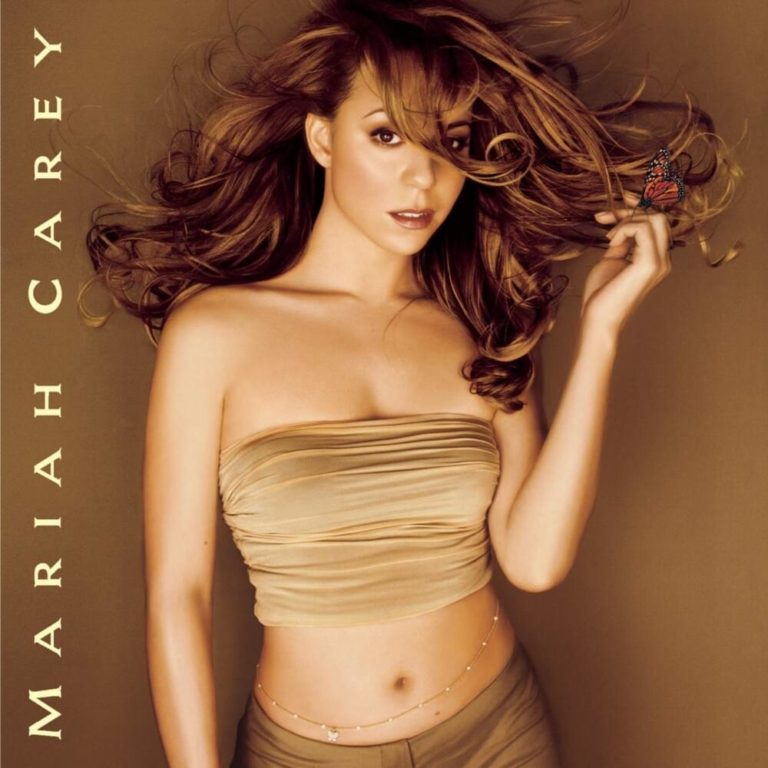 Mariah Carey in goldfarbenem Outfit mit Schmetterling auf der Hand vor braunem Hintergrund.
