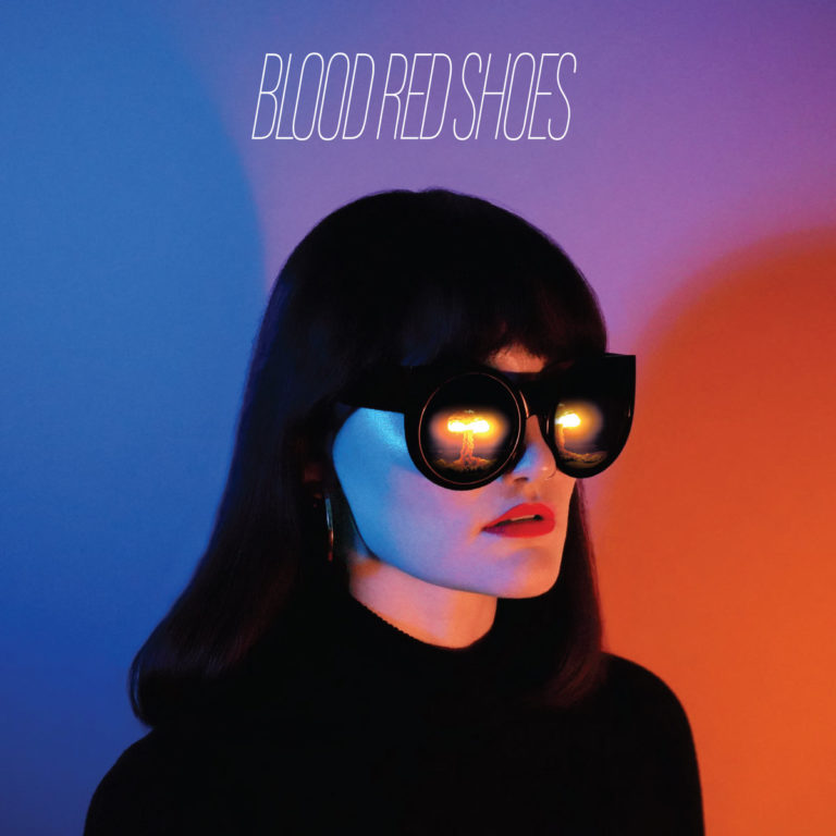 Albumcover von Ghosts On Tape zeigt eine Frau mit übergroßer Sonnenbrille, in der sich zwei Atompilze spiegeln – zwischen Neon, Apokalypse und Retro-Coolness.