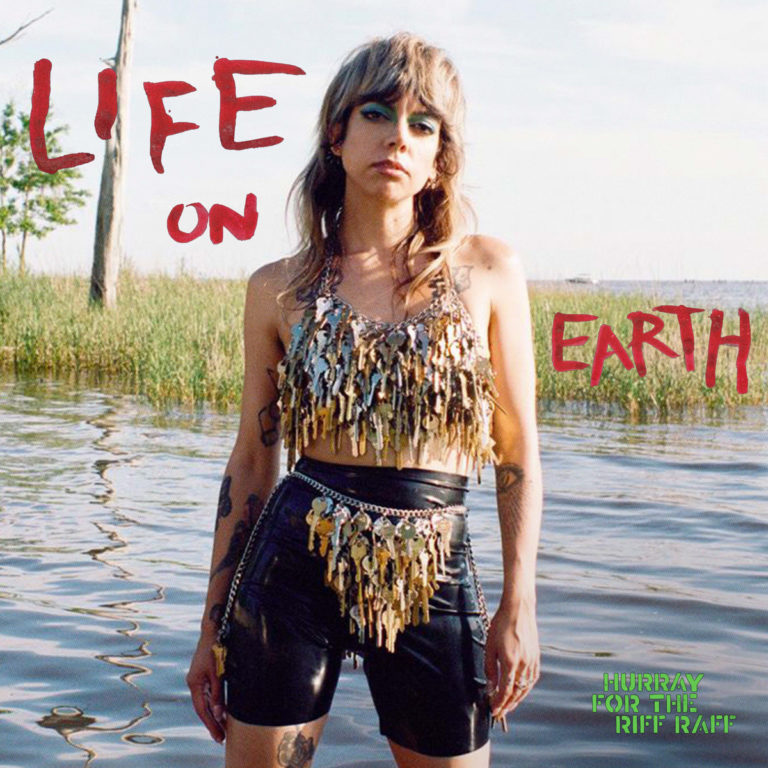 Cover des Albums „Life on Earth“ von Hurray for the Riff Raff – Alynda Segarra steht selbstbewusst im Wasser vor Schilf, trägt ein Oberteil und einen Gürtel aus glänzenden Schlüsseln, darüber in roter Handschrift der Albumtitel.