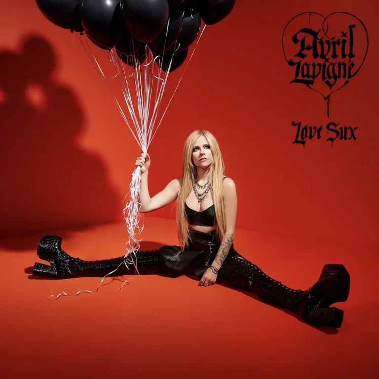 Avril Lavigne sitzt im Spagat vor knallrotem Hintergrund, hält einen Strauß schwarzer Luftballons, trägt Plateau-Boots, Leder-Outfit und entschlossenen Blick.