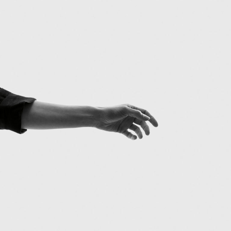 Schwarz-weißes Cover mit minimalistischem Design: Ein einzelner ausgestreckter Arm ragt von links ins Bild, die Hand wirkt suchend, fast schwebend.