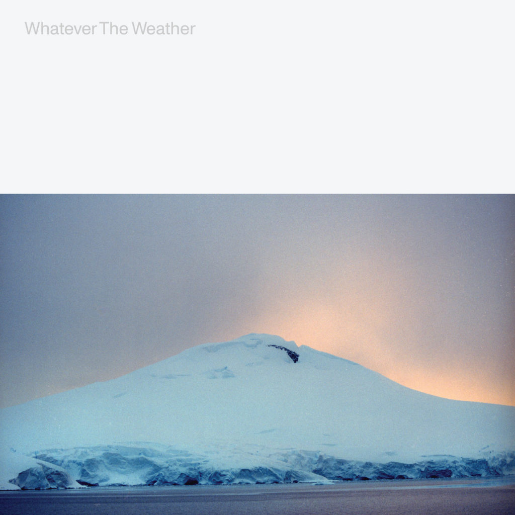 Panorama eines schneebedeckten Berggipfels bei Sonnenaufgang unter pastellfarbenem Himmel, darüber in heller Typografie „Whatever The Weather“.