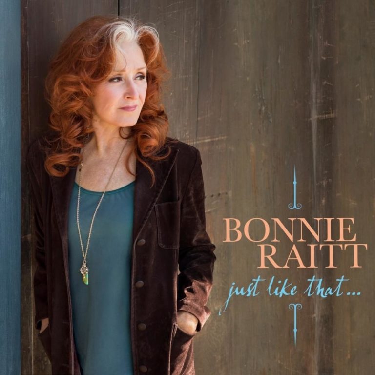 Bonnie Raitt lehnt in eleganter Pose an einer Säule, rotblondes Haar fällt über ihre Schulter, sie trägt eine schwarze Jacke und türkisfarbenes Top; rechts der Schriftzug „Just Like That…“.