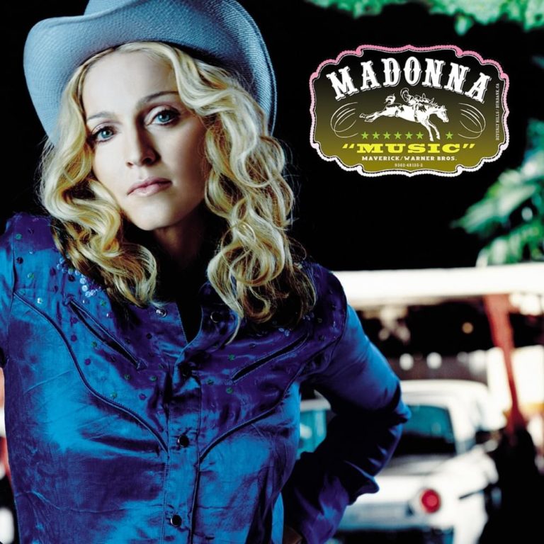Frau mit blonder Lockenfrisur und Cowboyhut in blauem Hemd vor dunklem Hintergrund.