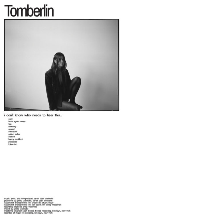 Schwarz-weiß-Porträt von Sarah Beth Tomberlin, sitzend vor einer hellen Wand, mit dem Schriftzug „Tomberlin“ oben links.