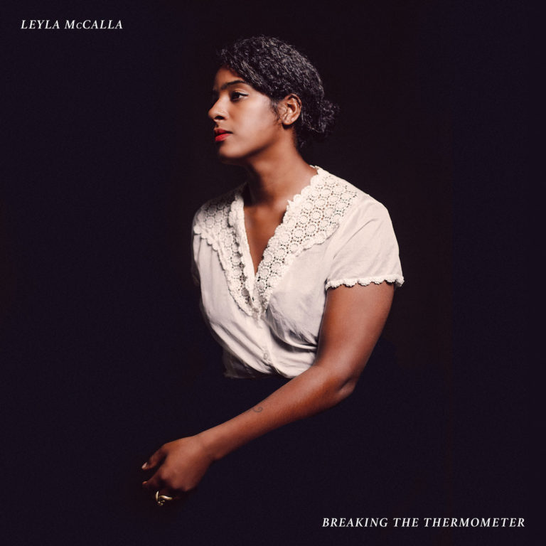 Leyla McCalla in traditioneller Bluse vor dunklem Hintergrund, nachdenklich zur Seite blickend – Cover von „Breaking the Thermometer“.