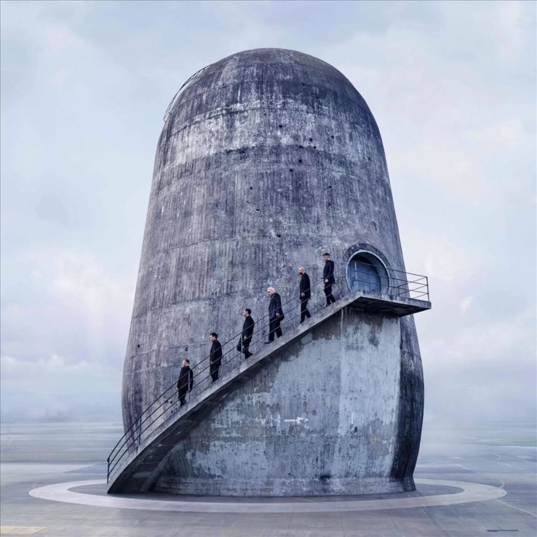 Sieben in Schwarz gekleidete Gestalten steigen eine Betonrampe an einem gigantischen, zylindrischen Turm empor – düsteres, postapokalyptisches Cover zu Rammsteins Album „Zeit“.